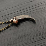 A bronze-colored canine tooth pendant necklace on a wooden surface.